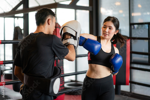 Young Asian woman boxer strikes with an elbow to professional trainer in boxing studuim in the background at fitness gym. Sporty fit for healthy lifestyle Asian model of boxing gym concept. © ake1150