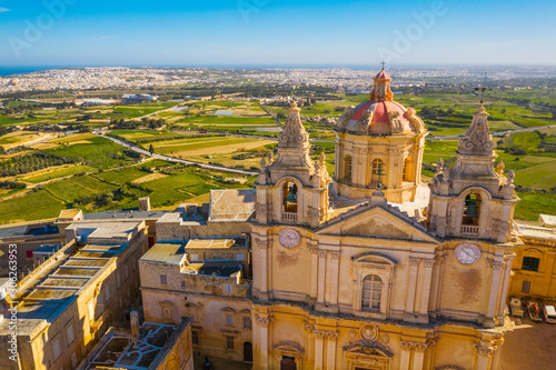 The main church and square in Mdina city - old capital of Malta. Aerial nature landscape, sunny day, blue sly, winter, a lot of green grass, field on background. Malta country