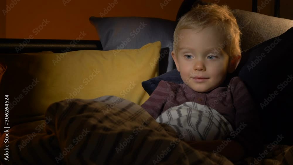 Child watching TV in dark bedroom before sleeping. Kid laying in bed, bedtime Child watching TV in dark bedroom before sleeping. Kid laying in bed, bedtime