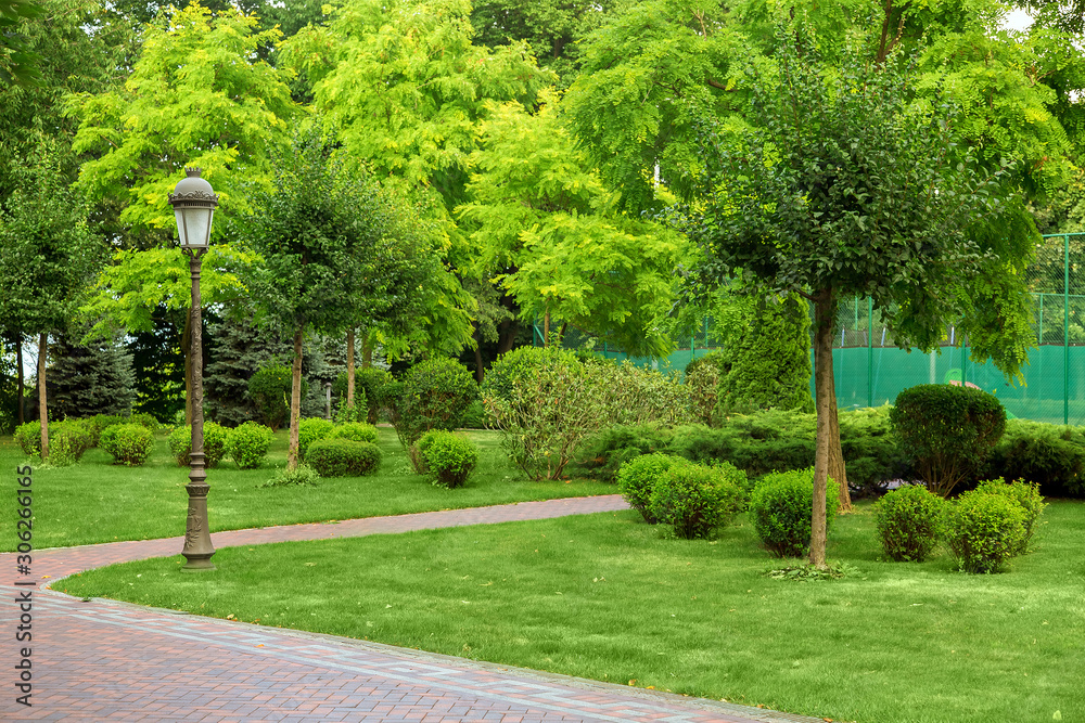 a park with pedestrian walkways with many different plants, an iron lantern on a summer day.