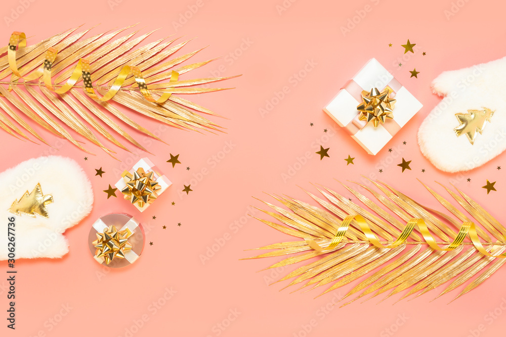 Obraz premium New year Christmas Stylish festive decorations concept, Golden palm leaves, white mittens, gift boxes, starry confetti, candles on pink background. Flat lay, copy space. Backdrop for greeting card