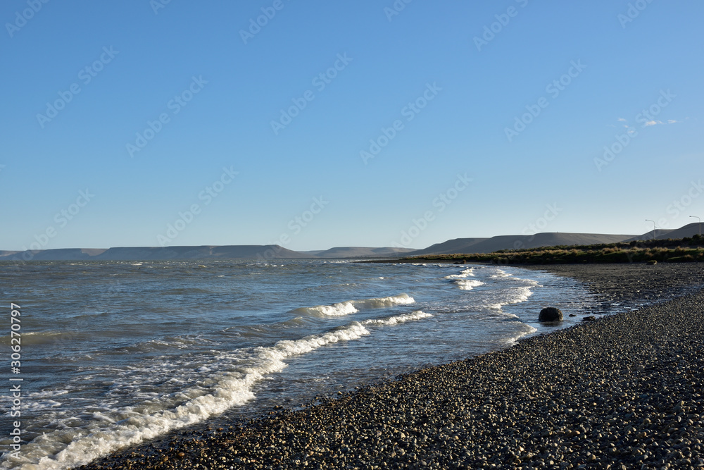 vista de playa con olas de marea subiendo y colinas bajo el cielo azul