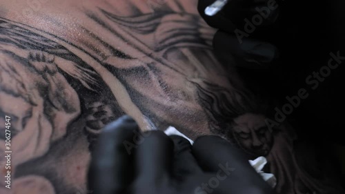 Close up tattoo artist demonstrates the process of getting black tattoo with paint on back of a client