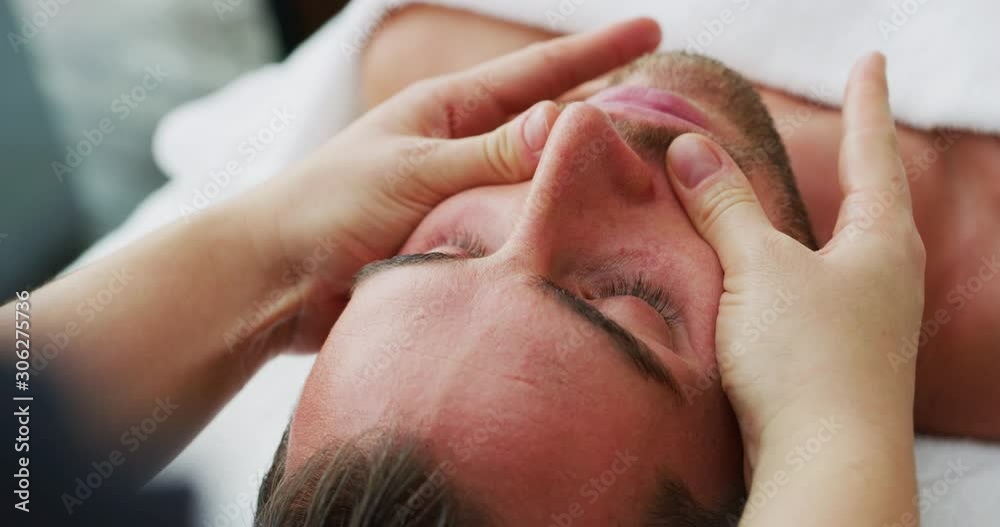 Close up of an young handsome man is receiving a facial massage and spa treatment for perfect skin in a luxury wellness center.