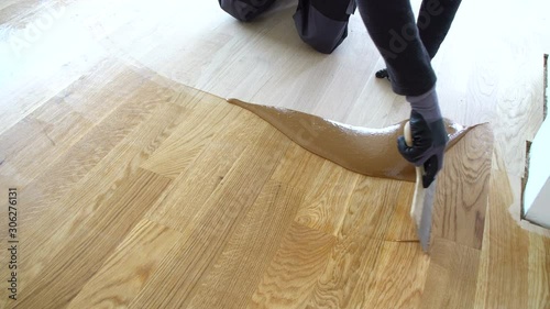 Carpenter master with gloves grouting wooden parquet, phase after sanding. Varnishing of oak parquet floor, man workers with hand and spatula