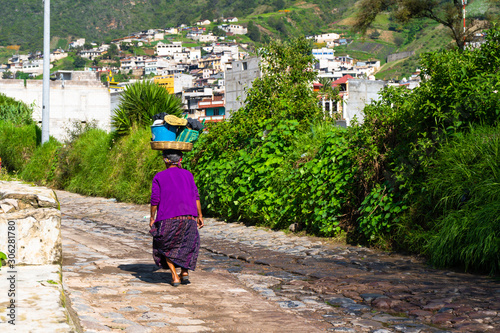 La señora está caminando con una cesta en la cabeza por una calle de Almolonga Guatemala. photo
