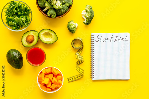 Diet program mockup. Start diet text in notebook near vegetables on yellow background top view