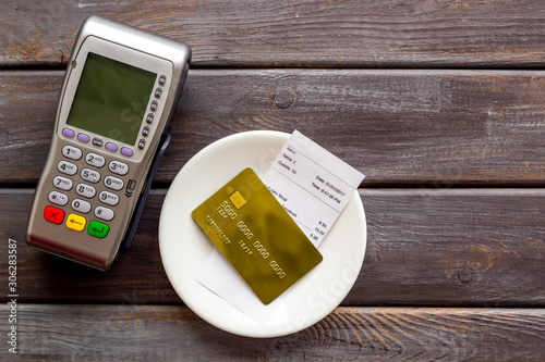 Electronic payments in restaurant. Bank card near aquiring terminal and bill on dark wooden background top view
