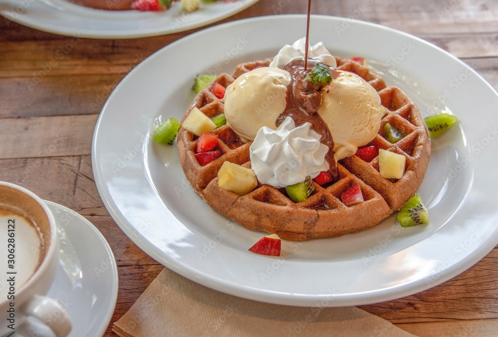 Chocolate sauce pouring on Belgian waffle with vanilla ice cream and fruits topping. Chocolate sauce pouring on Belgian waffle with vanilla ice cream and fruits topping.