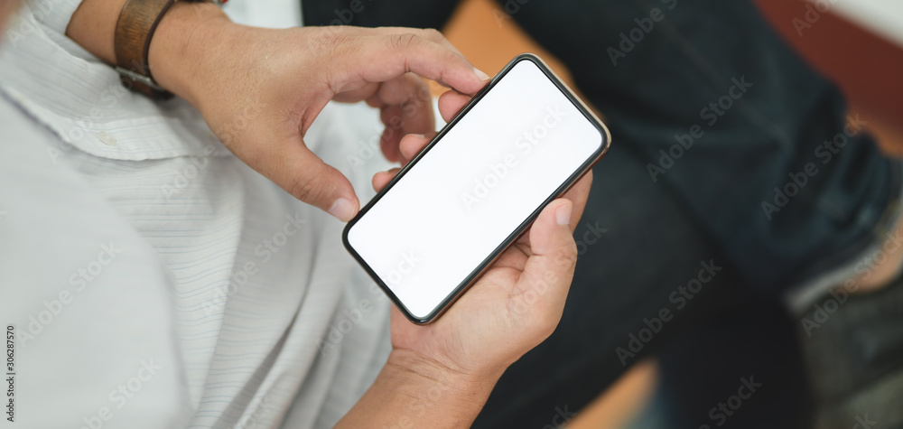 Cropped shot of man using his blank screen smartphone while sitting in comfortable room Cropped shot of man using his blank screen smartphone while sitting in comfortable room