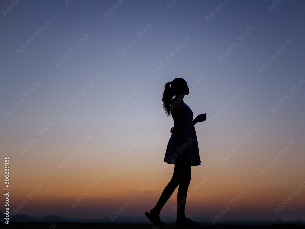 Silhouette of a young dancing woman with long wavy hair in the mountains , Natural light and darkness,against the background of the sunset sky.