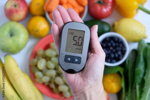 Diabetes concept: glucometer in hand and healthy food. Nutrition cause diabetic desease photo