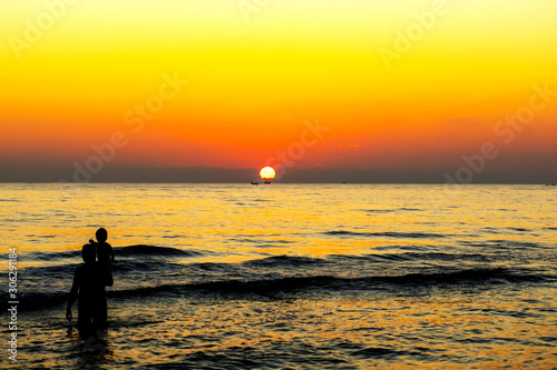 man stood by the sea with his familyin and watched the sun rise in the morning. He looked happy and warm 