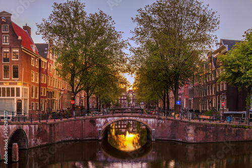 Fototapeta Light from the setting sun casts a golden glow over a canal in Amsterdam