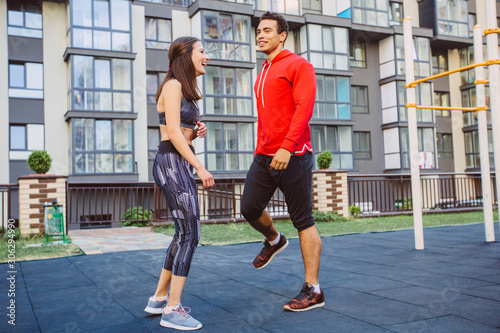 Young couple in black sports outfit doing morning workout outdoors. Young man and woman stretching they muscle before running on bridge.