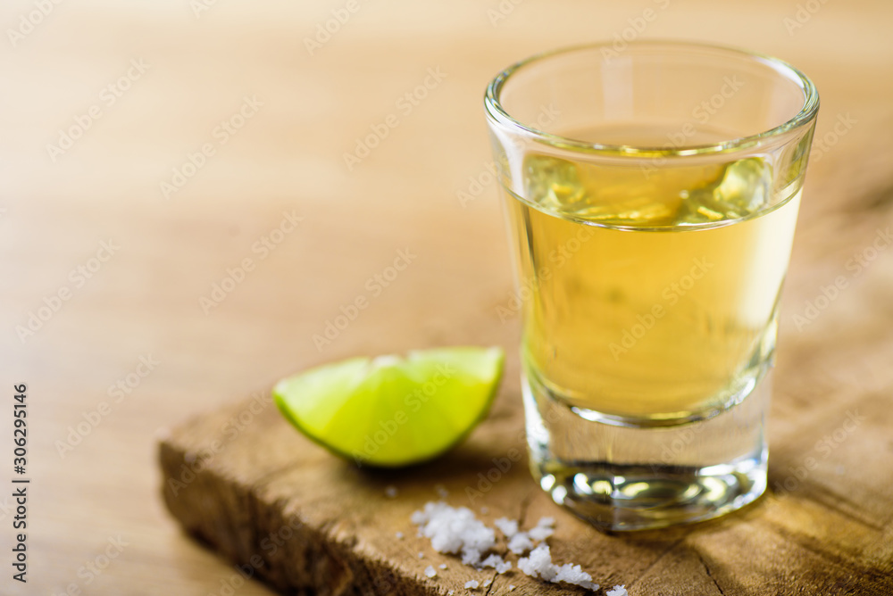 Fototapeta premium Tequila in a shot glass on a brown wooden background prepared for a party