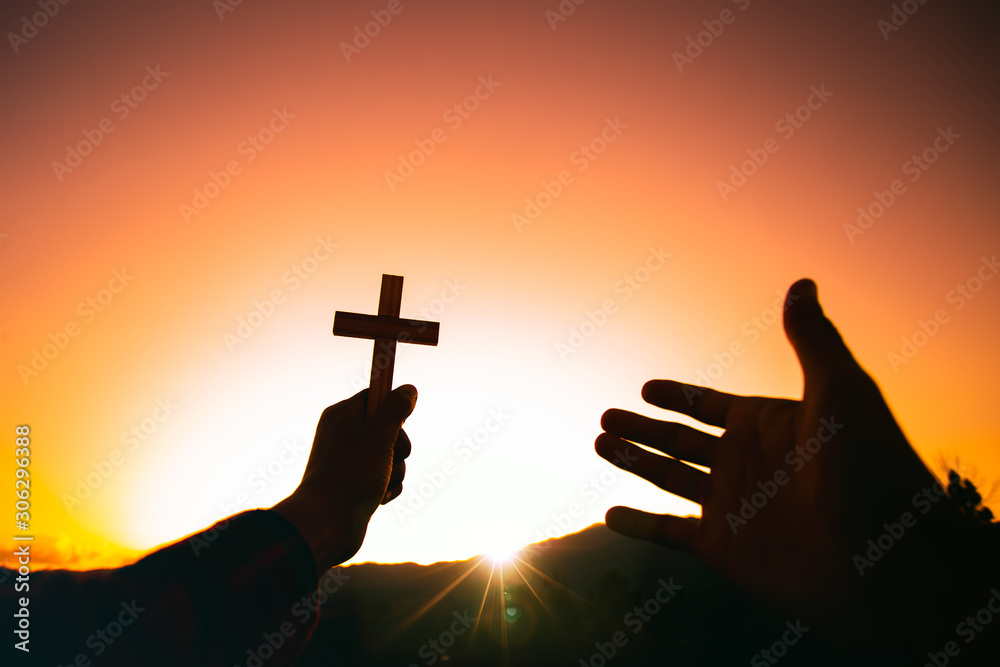 Human hand holding christian cross and praying with a sunset sky ...