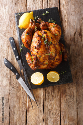 Juicy grilled chicken rotisserie with thyme, lemon closeup on a slate board. Vertical top view