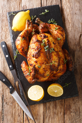 Tasty aromatic rotisserie chicken with thyme, lemon and spices close-up on a slate board. Vertical top view