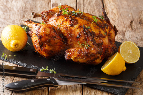 Juicy grilled chicken rotisserie with thyme, lemon closeup on a slate board. horizontal