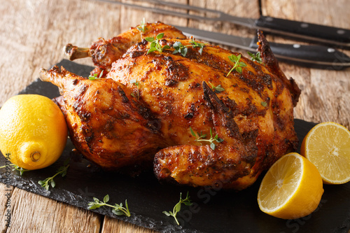 Tasty aromatic rotisserie chicken with thyme, lemon and spices close-up on a slate board. horizontal