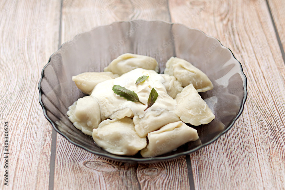 freshly cooked hot dumplings with sour cream and Basil in a dark plate on a wooden background