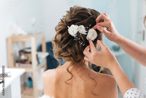 hairdresser makes an elegant hairstyle styling bride with white flowers in her hair photo