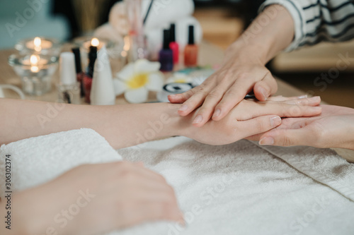 Beauty therapist doing manicure on hand of young asian woman in spa salon. closeup view of two female hands while beautician massage customer hands skin with moisturizing lotion before nail polishing