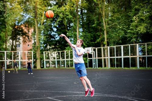 A young man throws a basketball on the city school Playground.