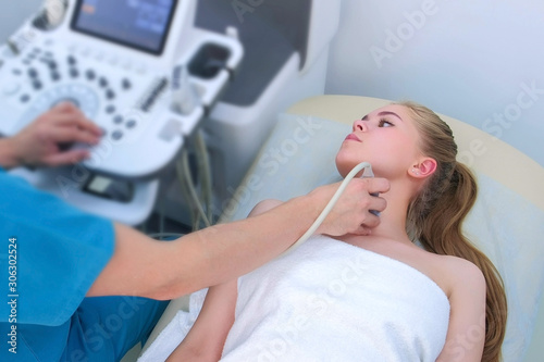 Man doctor examining patient s young woman thyroid gland using ultrasound scanner machine. Doctor runs ultrasound sensor over patient s neck and looking at screen. Diagnostic examination.