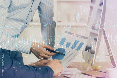 Double exposure of chart with businessman typing on computer in office on background. Concept of hard work.