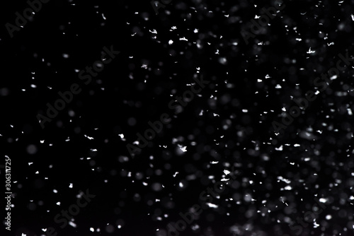 Falling snow at night. Bokeh lights on black background, flying snowflakes in the air. Overlay texture. Snowstorm