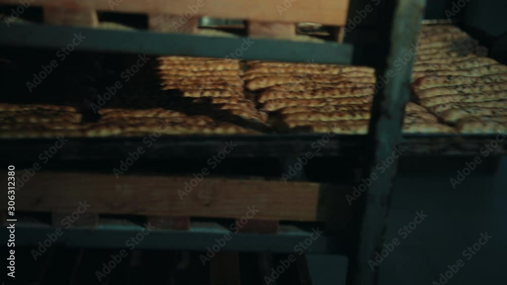 Baker hands in gloves push tray with long pastry baked sticks back in rack as shelf. Crispbead lies in rows, seasoned, sprinkled with cumin, caraway. Baker hands in gloves push tray with long pastry baked sticks back in rack as shelf. Crispbead lies in rows, seasoned, sprinkled with cumin, caraway.