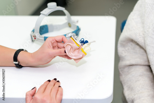 Doctor holding artificial human ear model shoving to the patient. Plastic colorful ear model. Medical theme or science classes.