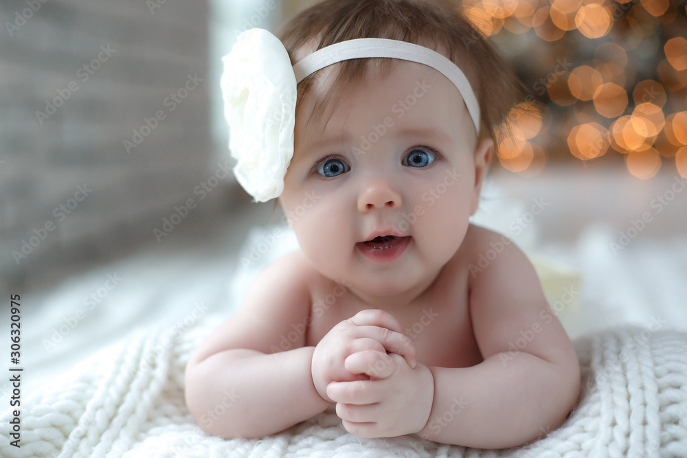 Lovely,beautiful newborn girl lying on a white blanket with a white flower on his head,new year and Christmas decorations.Portrait of a little girl with blue eyes against the background of a Christmas - obrazy, fototapety, plakaty 
