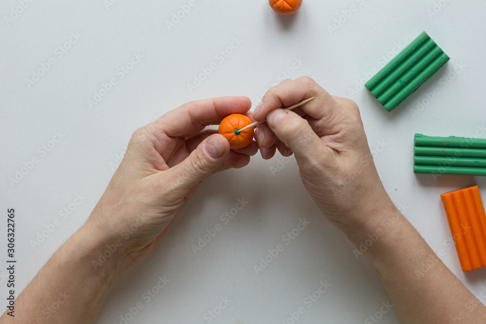 Woman hands putting green color on dot on orange ball to create orange fruit from polymer clay