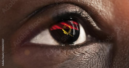 Woman black eye in close up with the flag of Angola in iris with wind motion. video concept