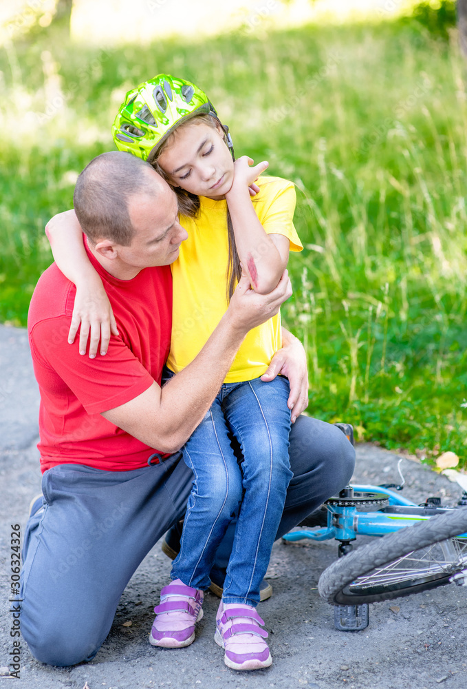 Fototapeta premium Father looks at the wound of his daughter, who fell from a bicycle