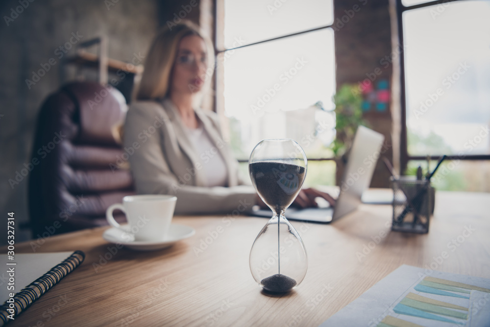 Photo of business woman looking at hourglass counting time till the end of the work day finishing her project in time Photo of business woman looking at hourglass counting time till the end of the work day finishing her project in time
