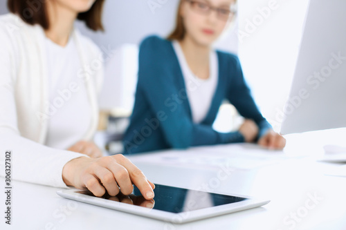 Businesswoman pointing at tablet computer screen while giving presentation to her female colleague. Group of business people working at the desk in office. Teamwork concept