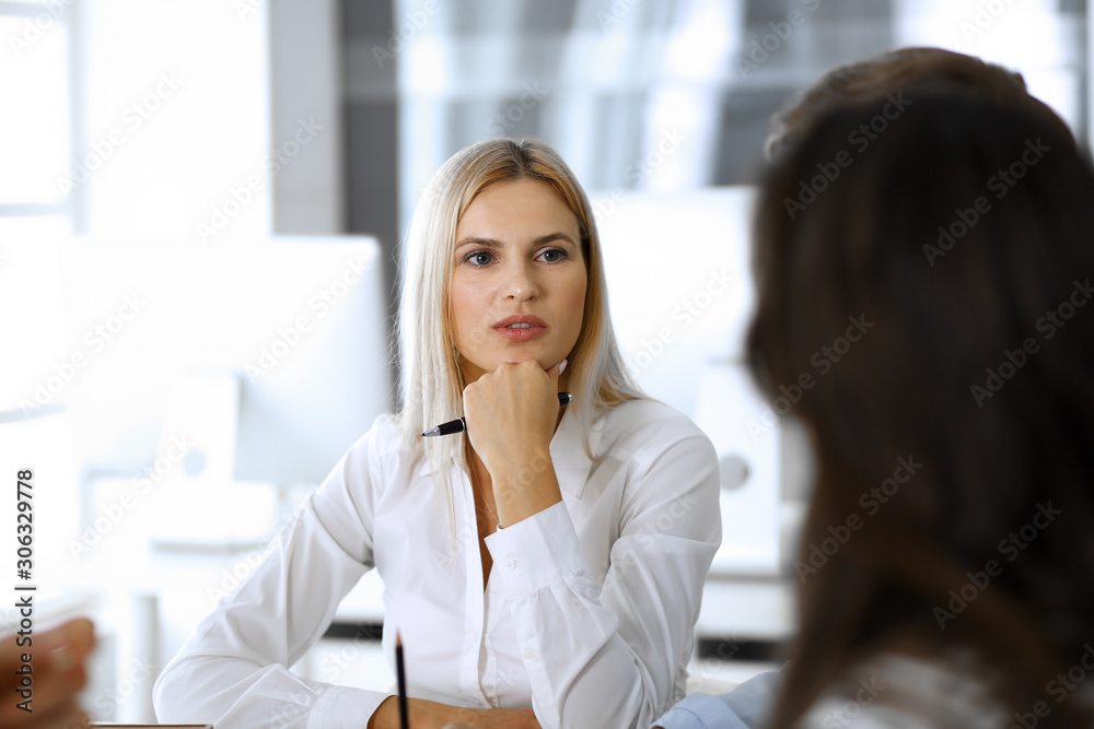 Group of business people discussing questions at meeting. Headshot of blonde businesswoman while smiling to her colleague at office negotiation. Teamwork and cooperation in corporate occupation Group of business people discussing questions at meeting. Headshot of blonde businesswoman while smiling to her colleague at office negotiation. Teamwork and cooperation in corporate occupation