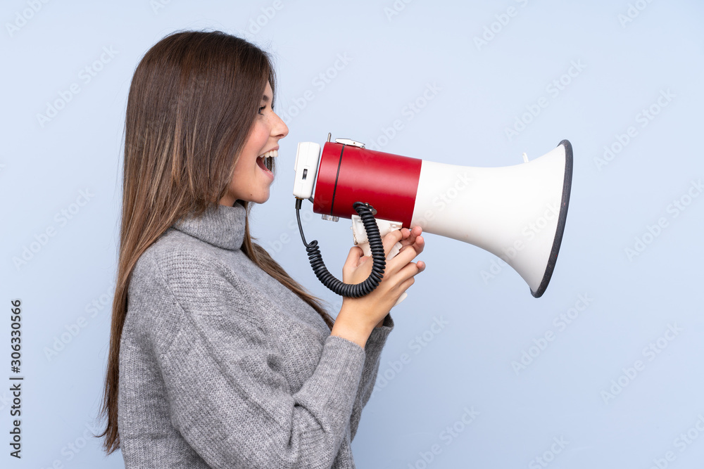 Teenager Brazilian girl over isolated blue background shouting through a megaphone Teenager Brazilian girl over isolated blue background shouting through a megaphone