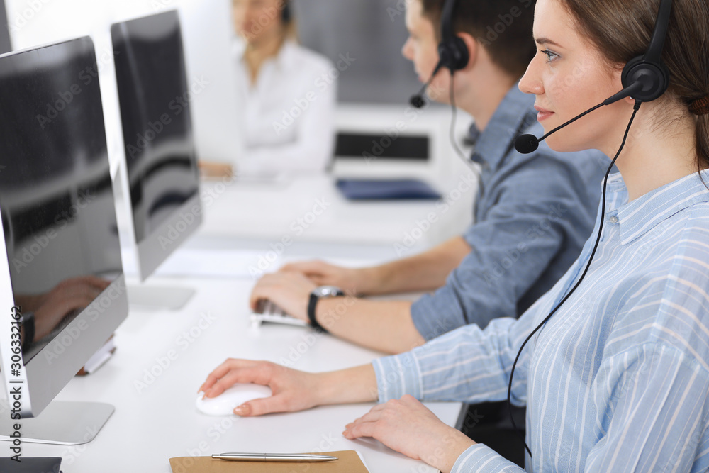 Fototapeta premium Call center. Group of casual dressed operators at work. Focus on business woman in headset at customer service office. Telesales in business