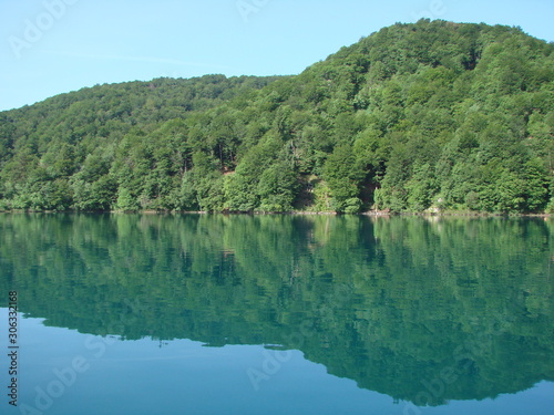 View from the deck of the ship on the quiet azure surface of the lake surrounded by mountain forest that densely covers its shores.