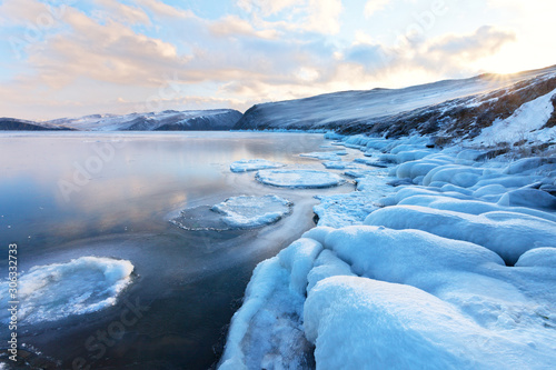 Beautiful winter landscape of freezing Baikal Lake at sunrise. Frosty morning on the shore of Strait Olkhonsky Gates. Icy stones and thin ice in the bay. Change of seasons, cold weather, climate