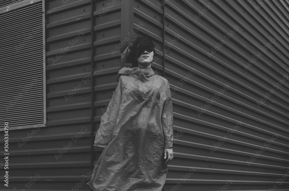 Black and white shot of Cute positive short haired women in red rain coat, Standing over green industrial wall