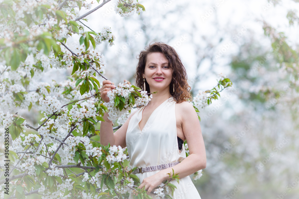 A portrait of beautiful young Caucasian woman with curly dark hair in blossoming orchard A portrait of beautiful young Caucasian woman with curly dark hair in blossoming orchard