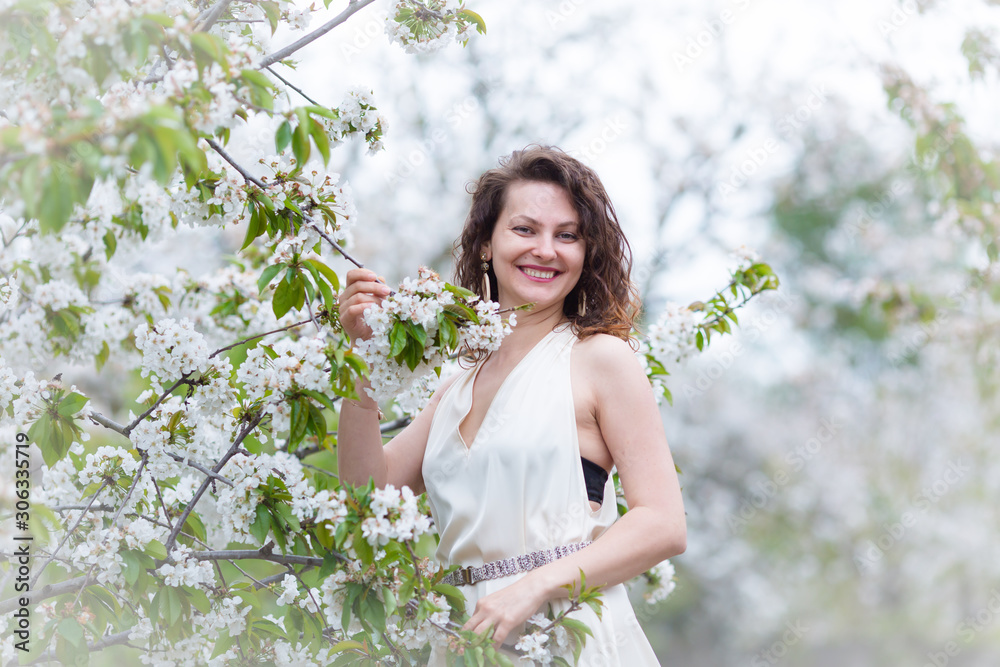 A portrait of beautiful young Caucasian woman with curly dark hair in blossoming orchard A portrait of beautiful young Caucasian woman with curly dark hair in blossoming orchard
