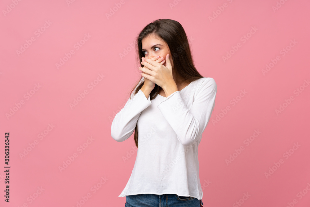 Young woman over isolated pink background covering mouth and looking to the side Young woman over isolated pink background covering mouth and looking to the side