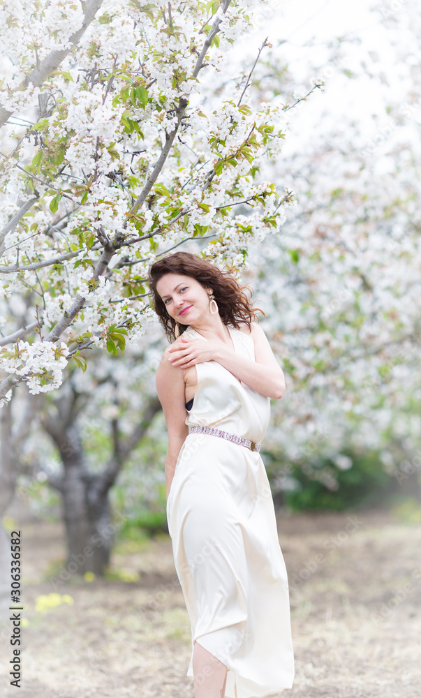 A portrait of beautiful young Caucasian woman with curly dark hair in blossoming orchard A portrait of beautiful young Caucasian woman with curly dark hair in blossoming orchard